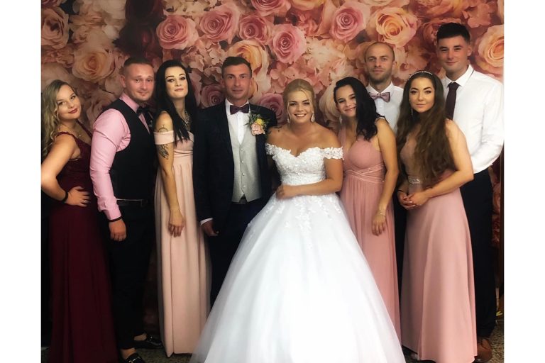 Nevesta so ženíchom a ich 7 priateľov v spoločenských šatách pred kvetinovým vynilovým fotopozadím rozmeru 290x230 cm