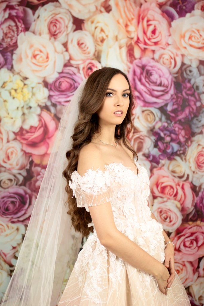 Detailnejší záber na nevestu v svadobných šatách pred kvetinovým fotopozadím