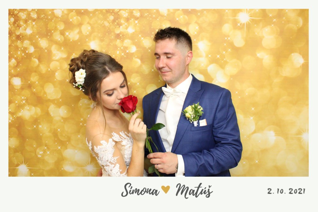 Mladomanželia Simona a Matúš pred zlatým fotopozadím pózujú s ružou.